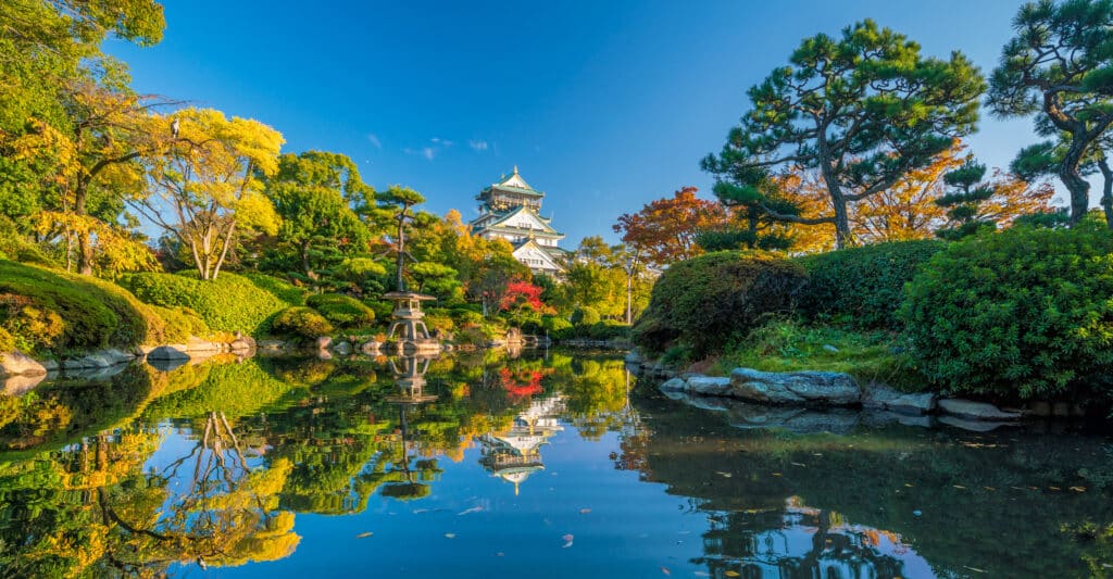 Osaka Castle surrounded by autumn trees reflected in a calm pond