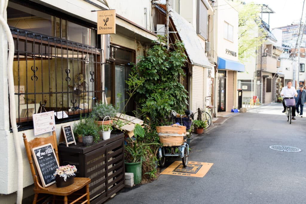 Quiet residential street in Osaka with small shops, plants, and a cyclist