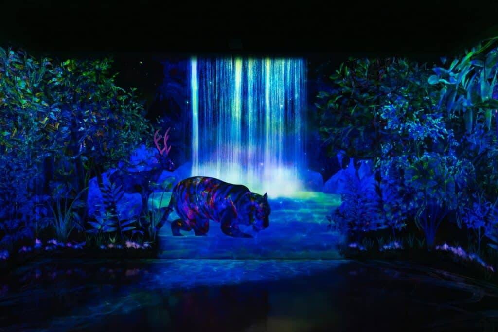 Immersive digital art installation at TeamLab Forest Fukuoka featuring illuminated waterfall and wildlife projections