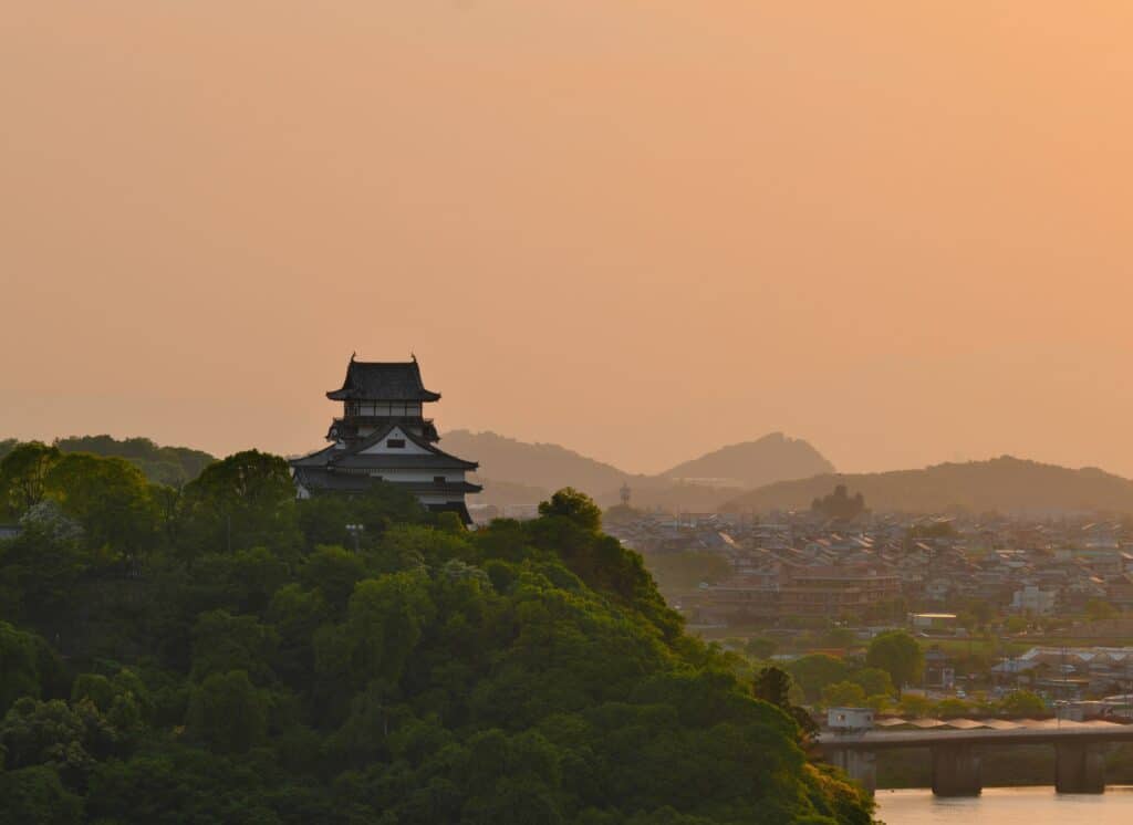 Inuyama Castle standing on a wooded hill overlooking the surrounding landscape at sunset