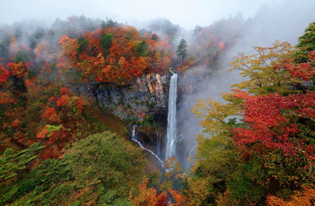 Kegon Falls in Nikko surrounded by colorful autumn foliage and misty mountain scenery