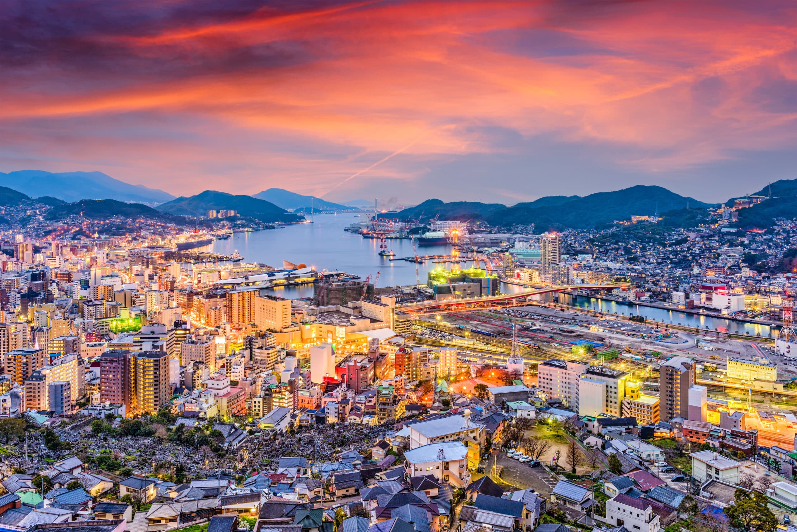Panoramic sunset view over Nagasaki city and harbor from a hillside viewpoint with colorful evening sky