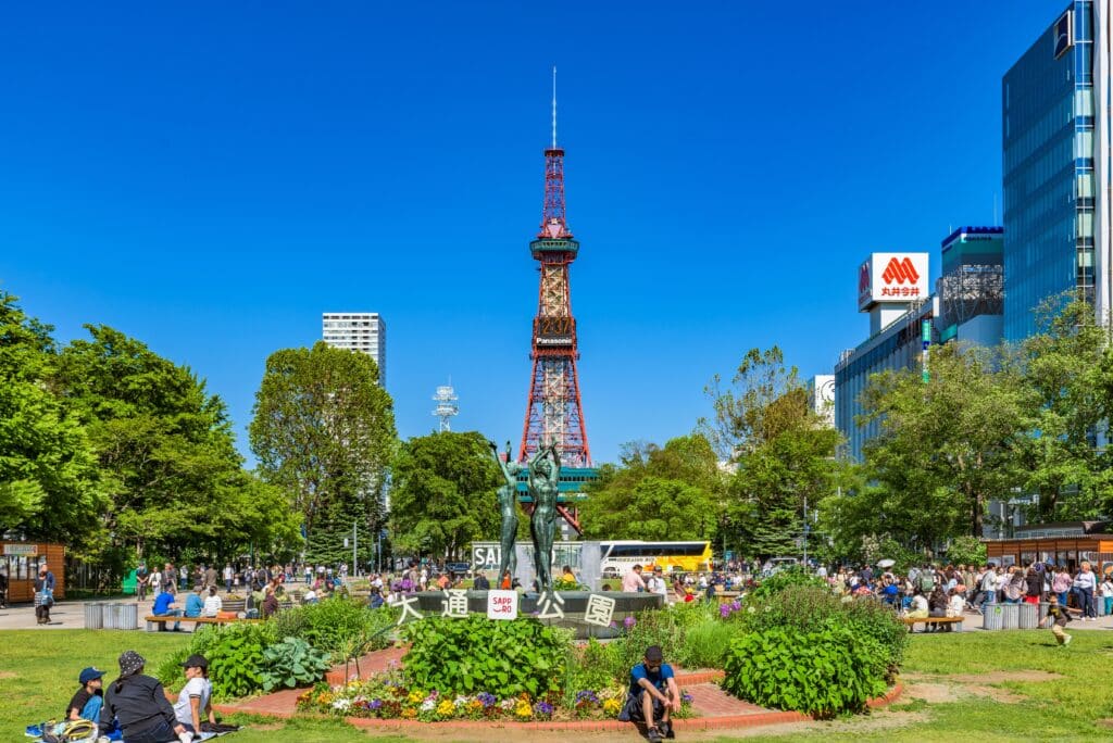 Visitors relaxing in Odori Park with the Sapporo TV Tower rising above downtown Sapporo