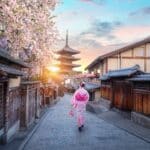 Traveler wearing a pink kimono walking through Kyoto's historic Higashiyama district toward Yasaka Pagoda during cherry blossom season