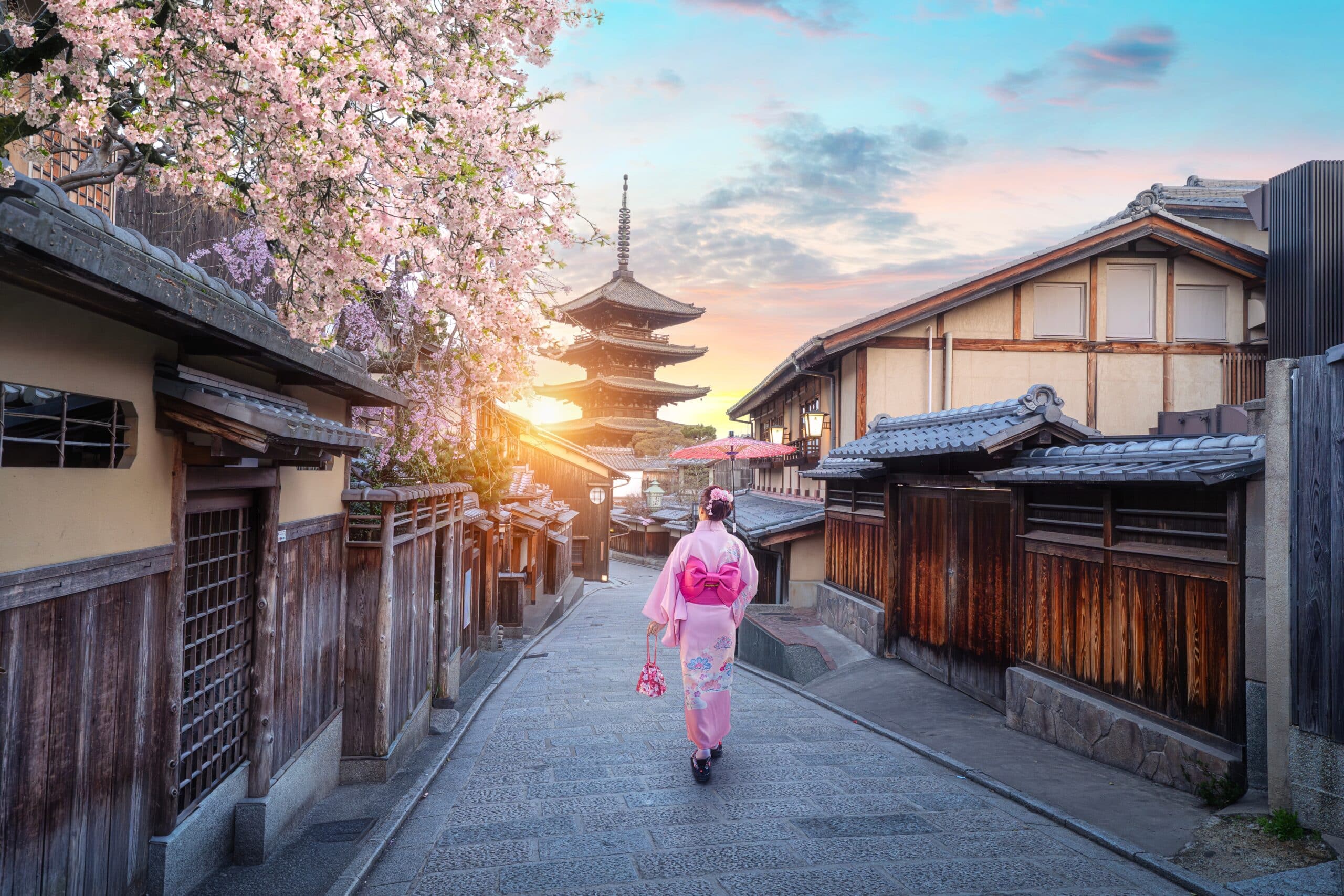 Traveler wearing a pink kimono walking through Kyoto's historic Higashiyama district toward Yasaka Pagoda during cherry blossom season