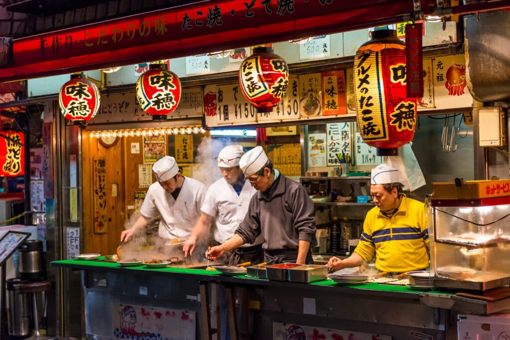 Chefs preparing fresh takoyaki at a traditional Osaka street food stall at night