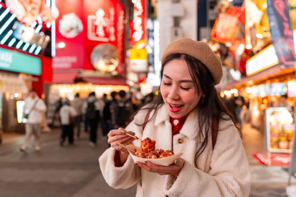 Traveler enjoying fresh takoyaki in Osaka's Dotonbori district at night