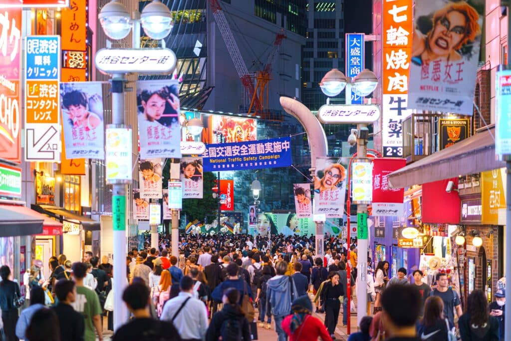Busy shopping street in Shibuya, Tokyo, filled with pedestrians and bright storefronts at night