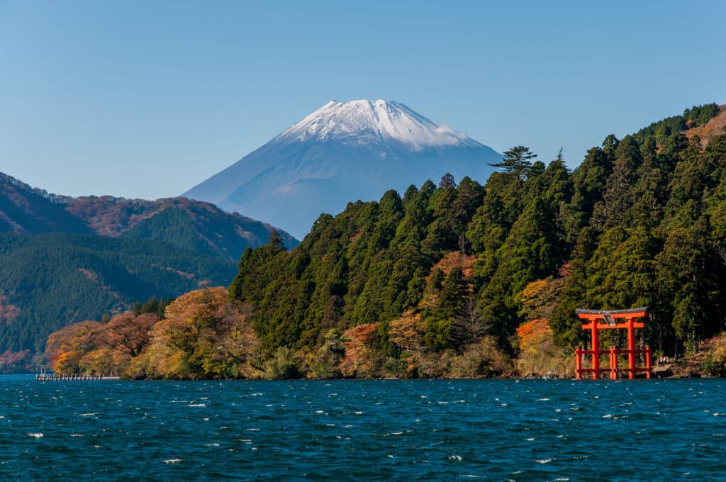 Mount Fuji rising behind forested mountains and the red Hakone Shrine torii gate beside Lake Ashi