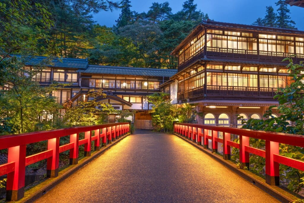 Traditional Japanese ryokan illuminated at dusk with a red bridge and wooden buildings