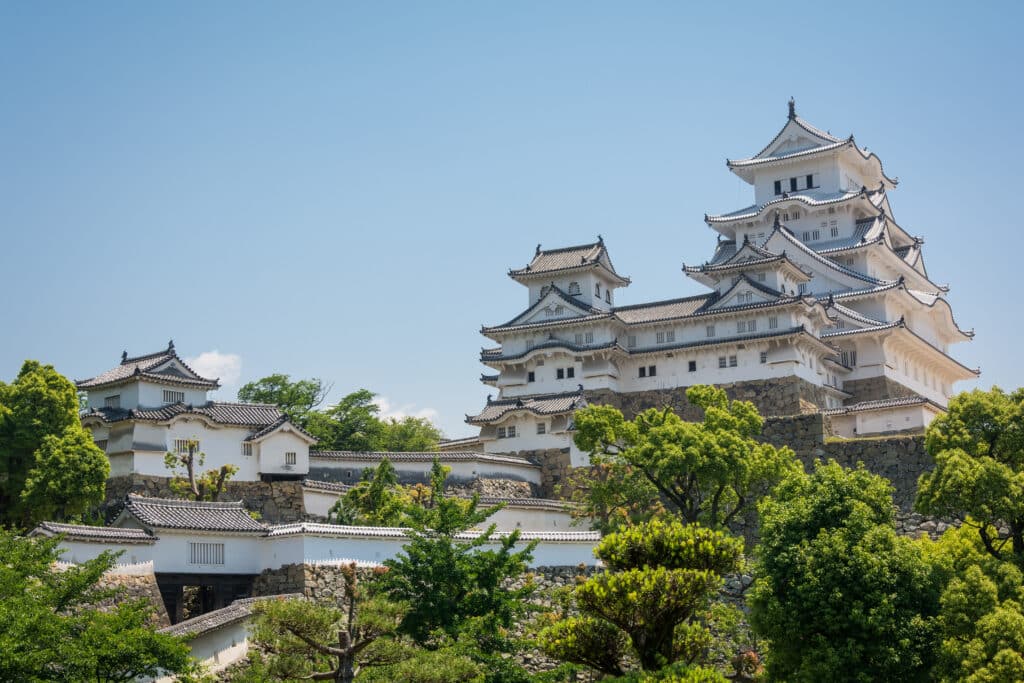 White towers of Himeji Castle rising above stone walls and green trees in Japan