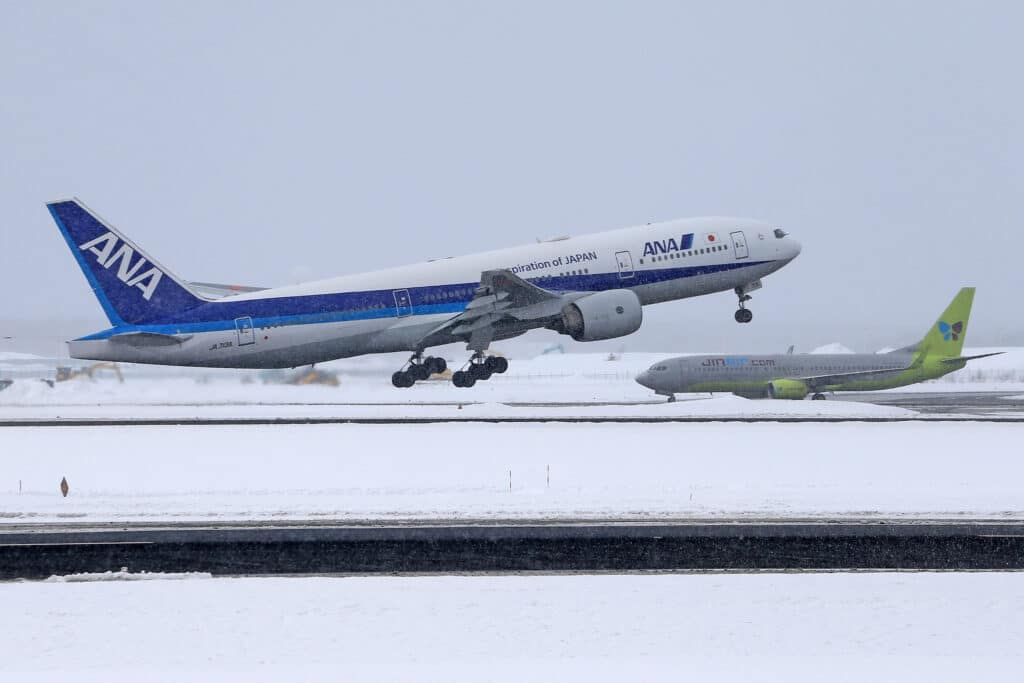 ANA passenger aircraft taking off from a snow-covered Japanese airport, with another aircraft in the background