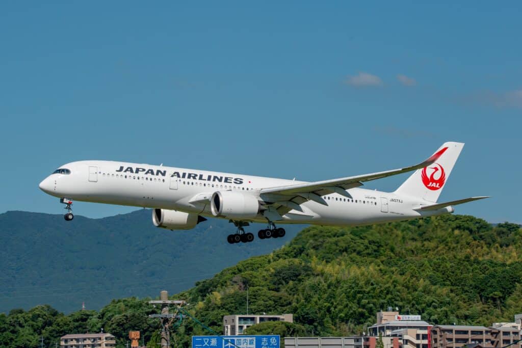 Japan Airlines passenger aircraft approaching an airport above green hills and buildings in Japan