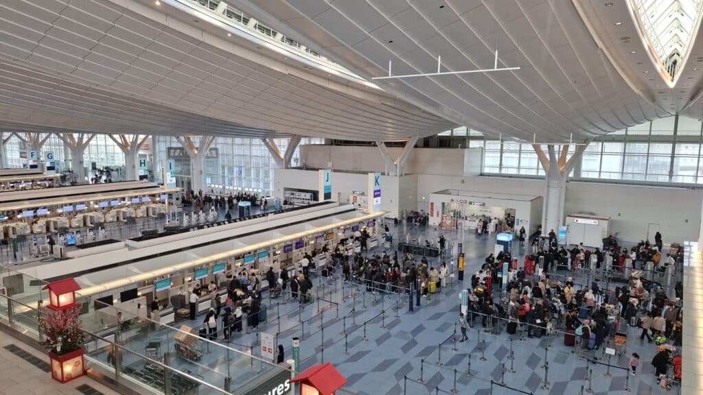 Spacious Japanese airport terminal with airline check-in counters, passengers, and luggage queues