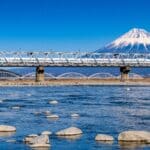 Shinkansen bullet train crossing a bridge with snow-covered Mount Fuji in the background