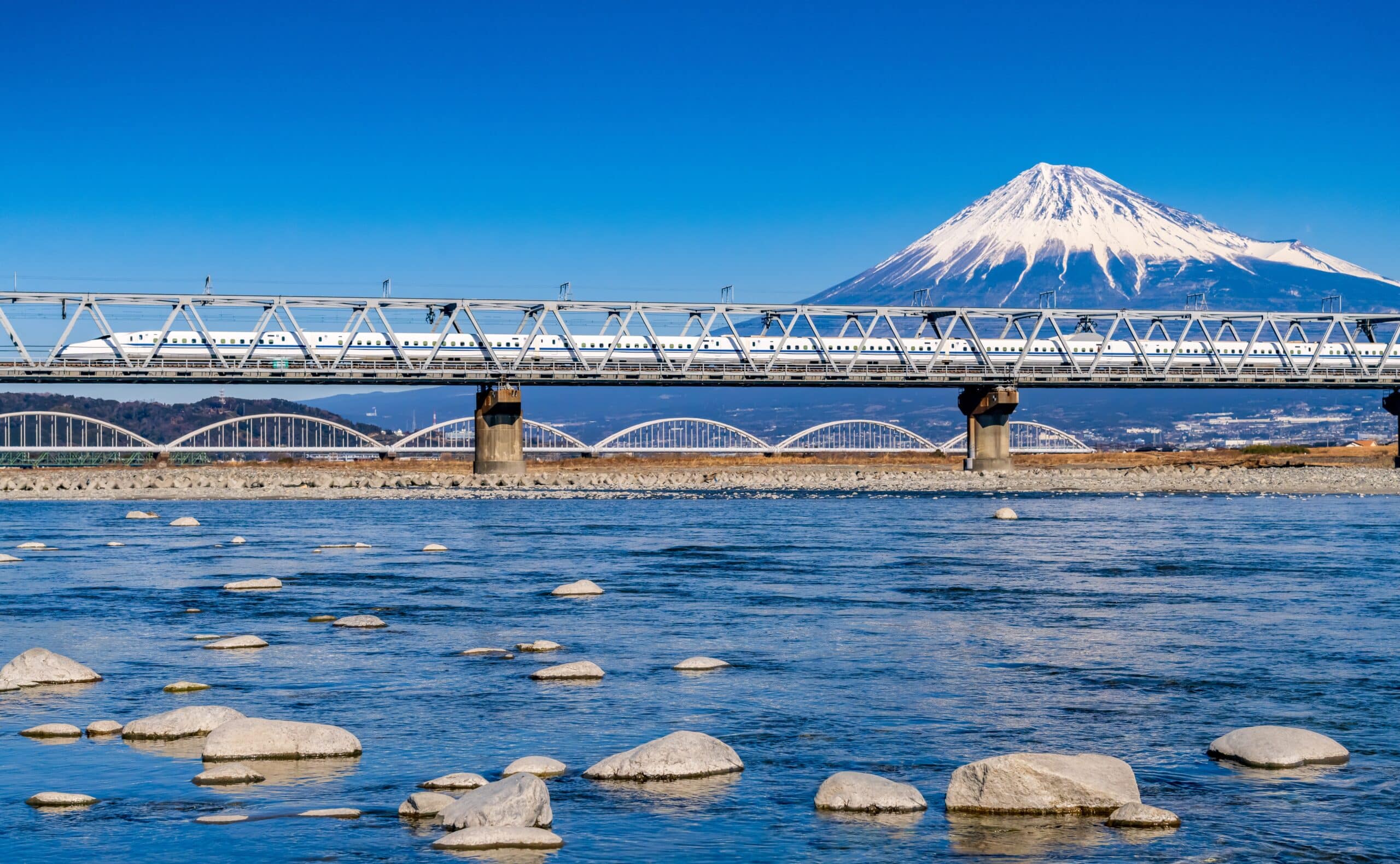 Shinkansen bullet train crossing a bridge with snow-covered Mount Fuji in the background