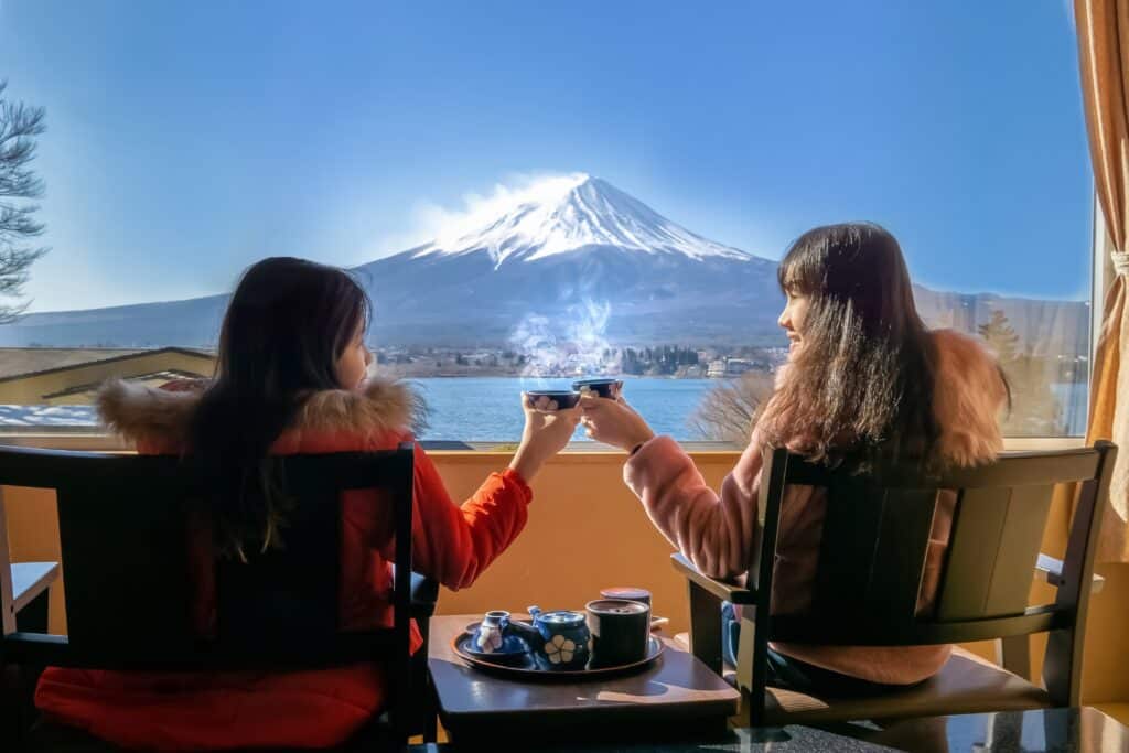 Two women enjoying hot tea beside a large window overlooking Mount Fuji and Lake Kawaguchi