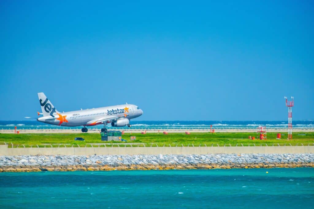 Jetstar passenger aircraft taking off beside turquoise coastal waters at an airport in Japan