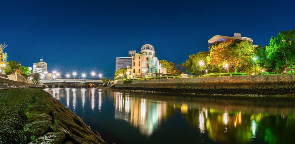 Hiroshima Atomic Bomb Dome illuminated at night beside the Motoyasu River, with city lights reflected in the water