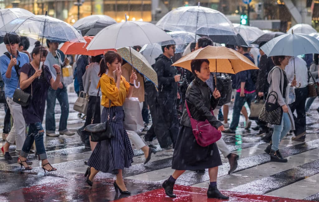 Pedestrians carrying umbrellas across a wet Japanese city street during heavy rainfall