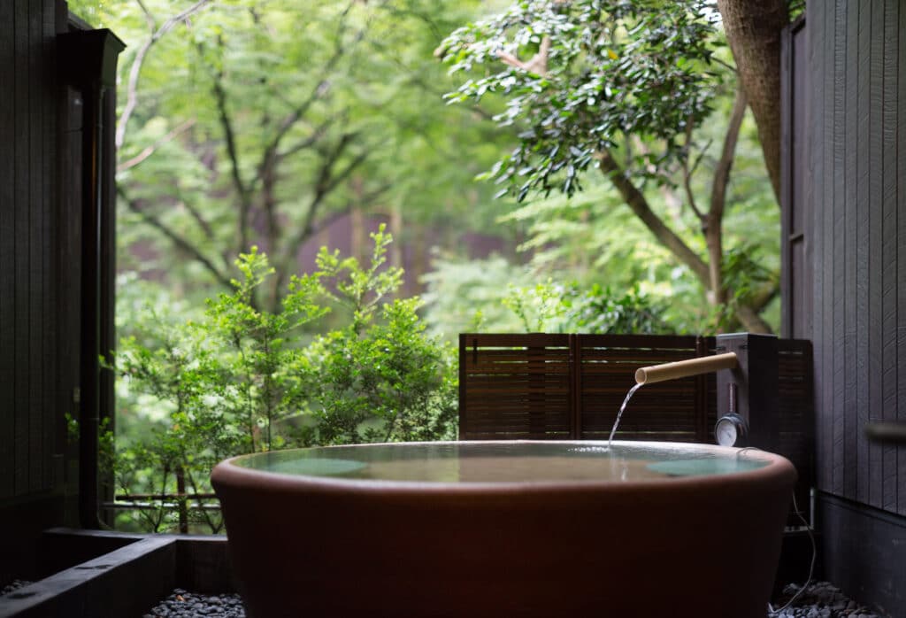 Private open-air Japanese onsen bath surrounded by lush green trees at a traditional ryokan