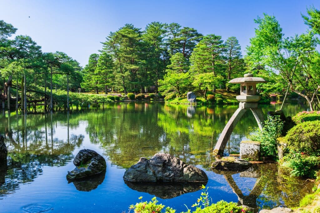 Traditional stone lantern beside a peaceful pond surrounded by green trees in Kenrokuen Garden, Kanazawa