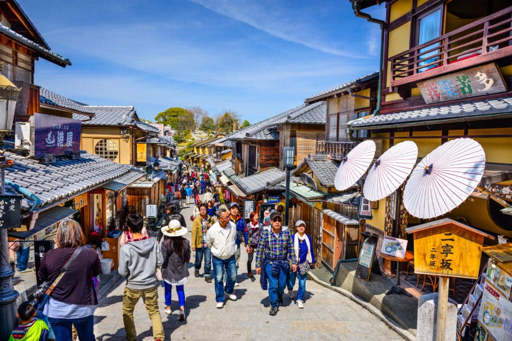Tourists walking along a crowded traditional shopping street in Kyoto's historic Higashiyama district