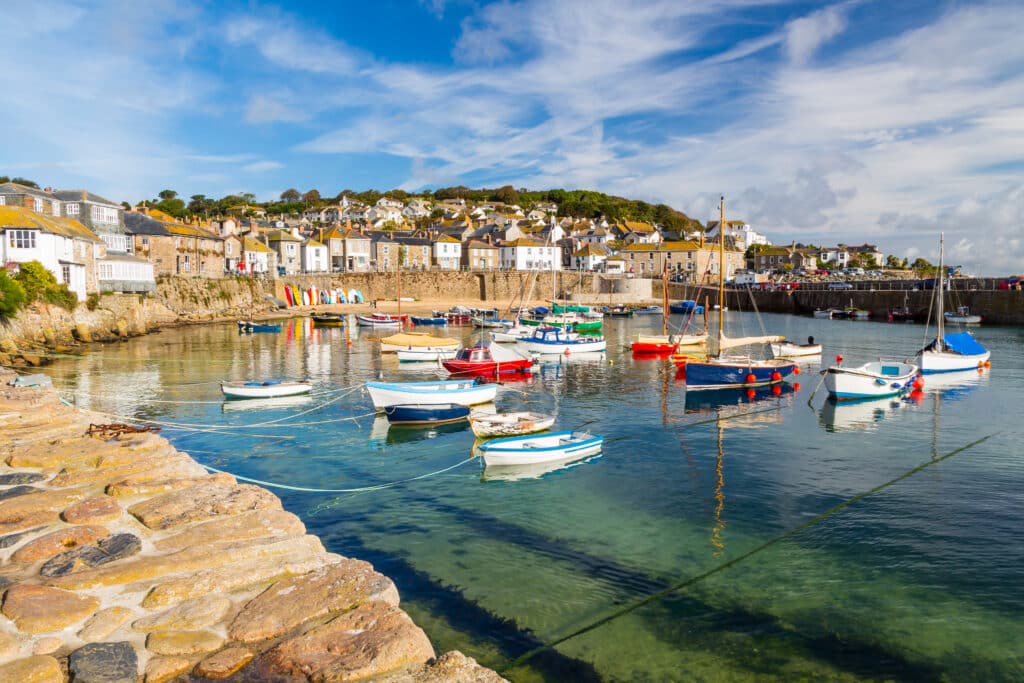 Mousehole harbour in Cornwall, with colourful fishing boats, traditional stone cottages and calm blue water