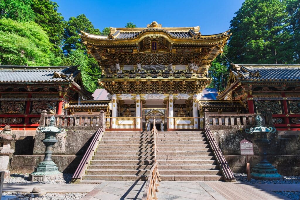 Ornately decorated Yomeimon Gate at Nikko Toshogu Shrine, with golden carvings and stone steps surrounded by trees