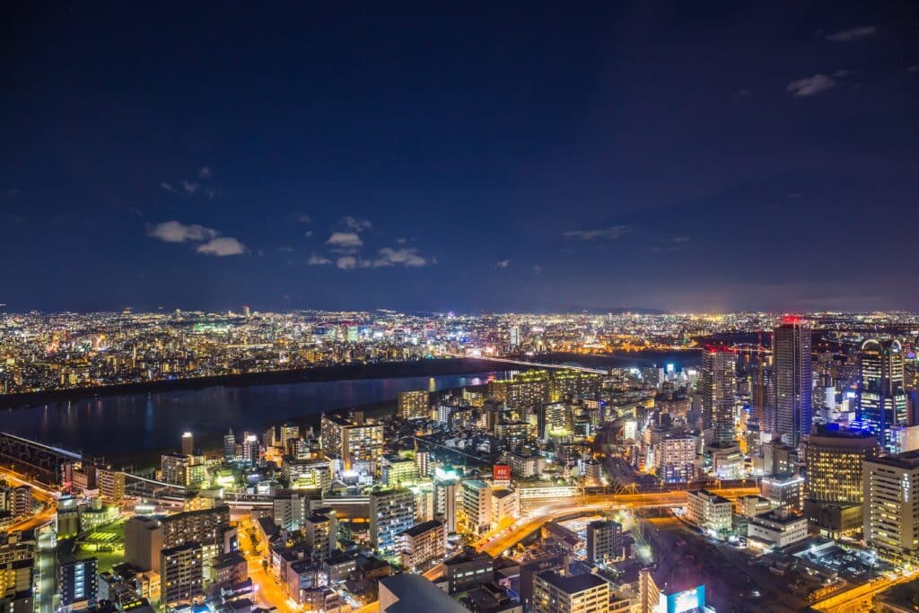 Panoramic nighttime view of Osaka's illuminated skyline, river, bridges, and high-rise buildings