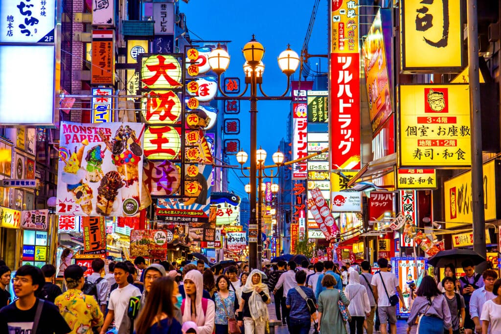 Crowded shopping and entertainment street in Osaka with colorful illuminated signs and restaurants