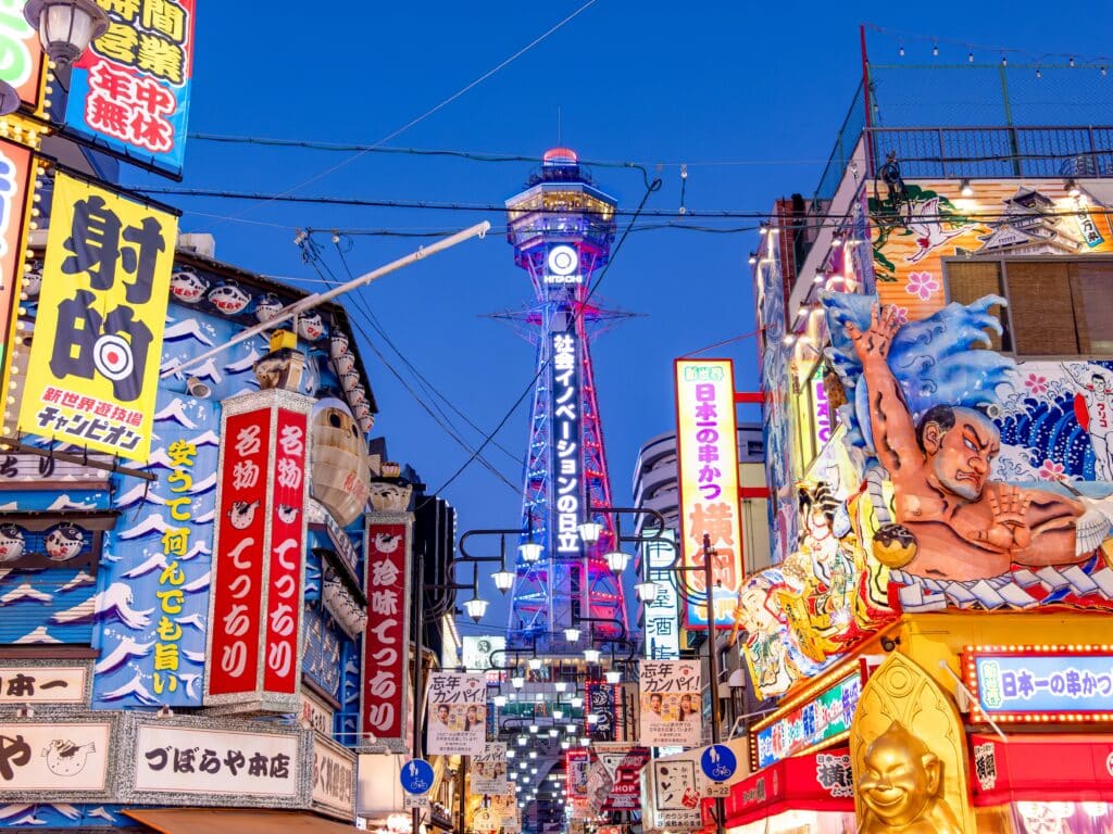Tsutenkaku Tower rising above colorful restaurant signs and illuminated streets in Osaka's Shinsekai district