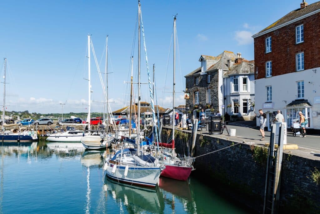 Padstow harbour in North Cornwall, with sailing boats, traditional stone buildings and visitors walking along the waterfront