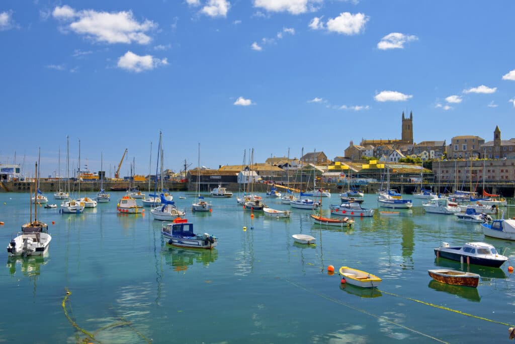 Fishing boats and sailing yachts in Penzance harbour, Cornwall, with historic buildings and a church tower in the background