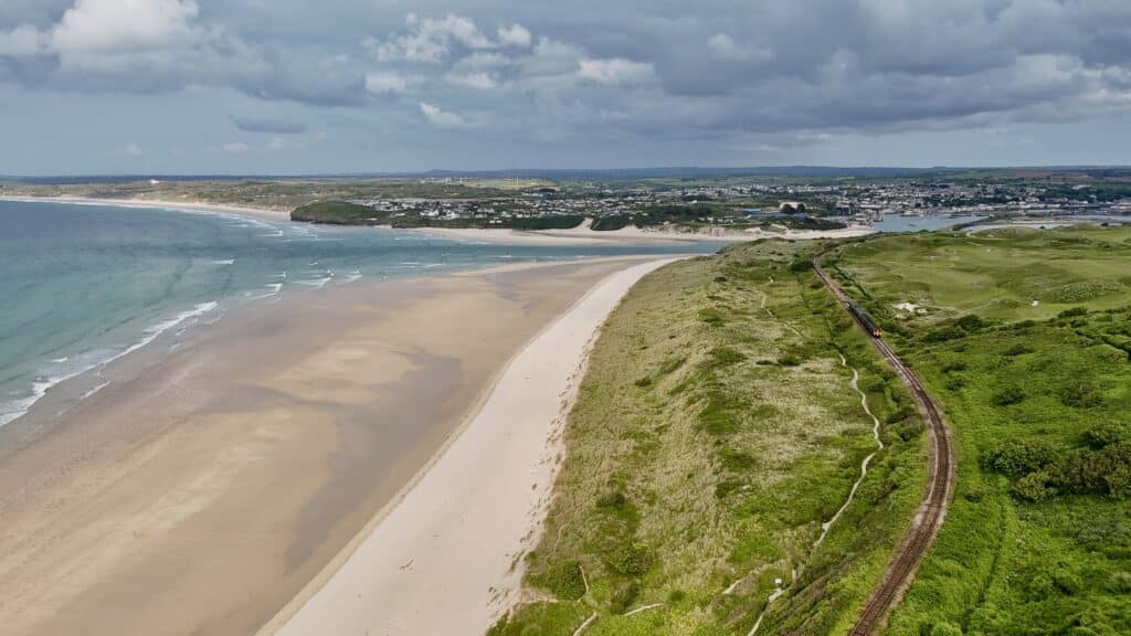A train travelling along the St Ives Bay railway beside sandy beaches and coastal dunes in Cornwall