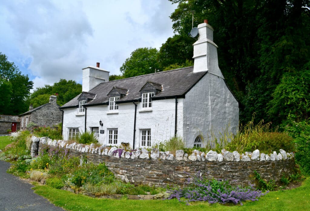 Traditional whitewashed Cornish cottage with a slate roof, stone garden wall and flowers