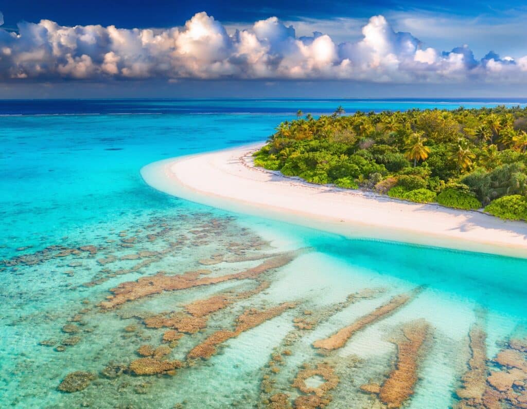 Aerial view of a tropical island with white sand, palm trees, and turquoise lagoon water